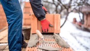 A builder with gloved hands constructs a brick wall during the winter