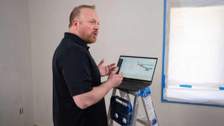 Customer discusses Buildxact with his laptop perched on a ladder